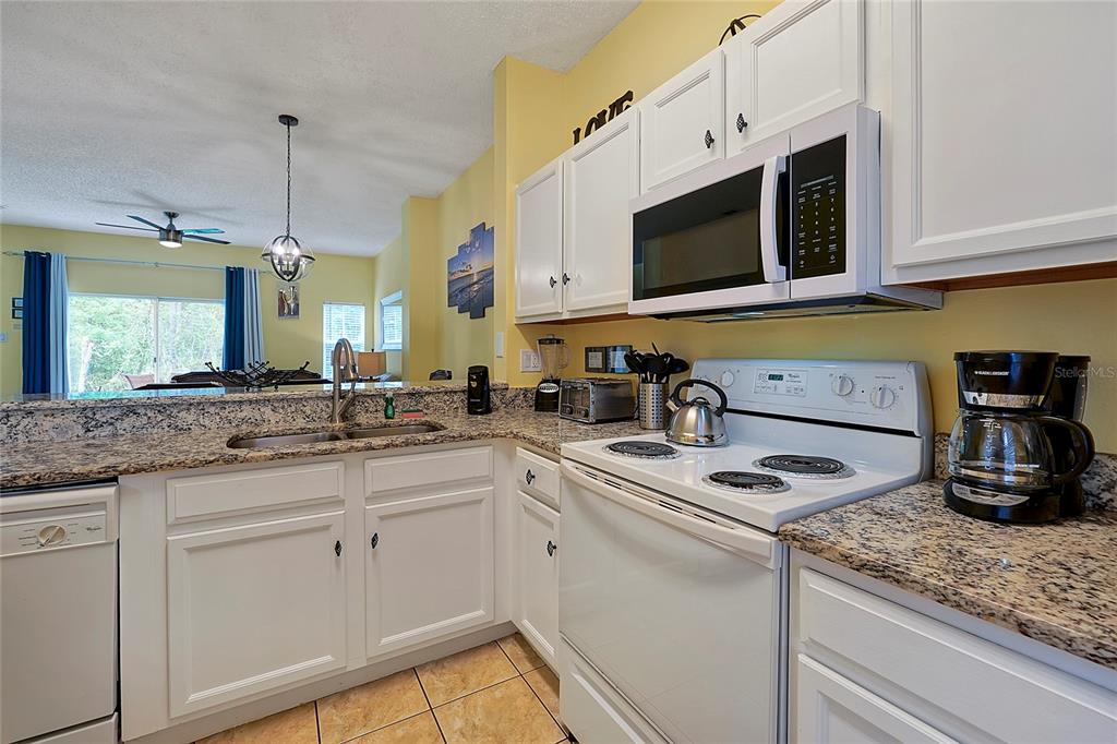 A kitchen features white cabinets, granite countertops, a white stove, and a stainless steel sink — 2767 SUN KEY PLACE, KISSIMMEE, FL