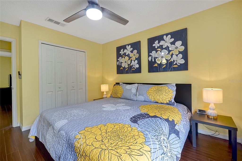 A bedroom features yellow walls, a bed with floral bedding, and a ceiling fan — 2767 SUN KEY PLACE, KISSIMMEE, FL