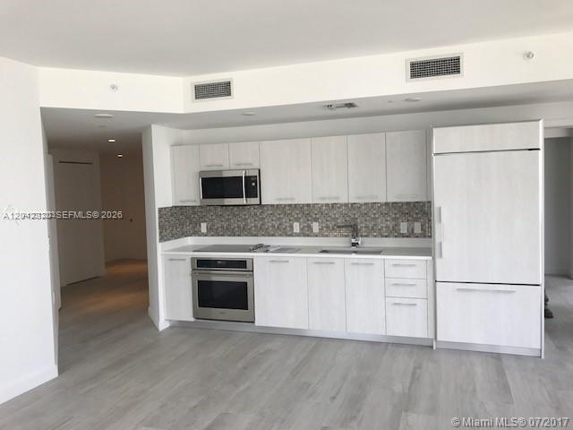 A modern kitchen features light wood cabinetry, stainless steel appliances, and a mosaic tile backsplash — 55 SW 9th St # 2103, Miami FL 33130, MIAMI, FL