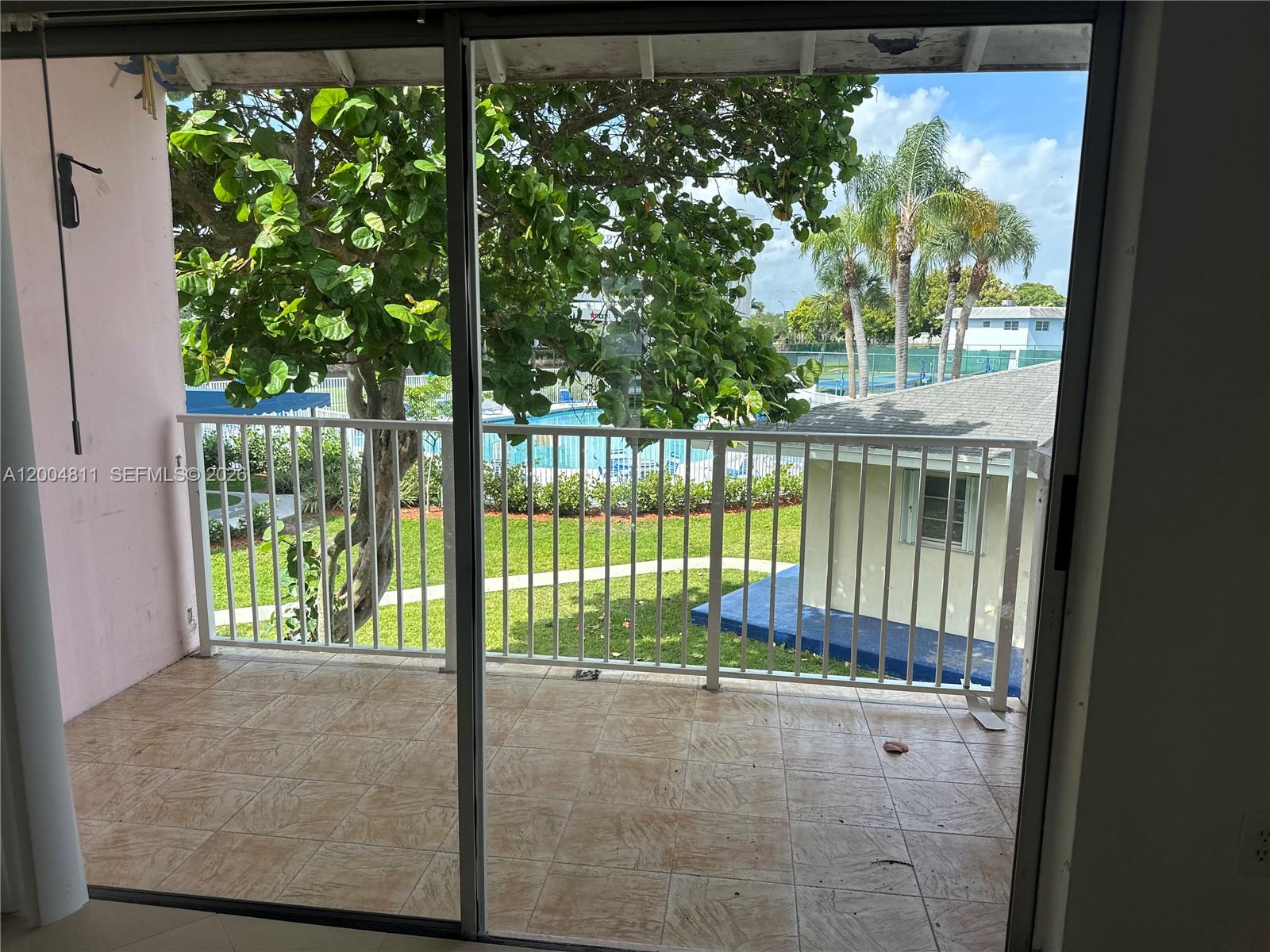 A tiled balcony overlooks a swimming pool, green lawn, and trees through a sliding door — 7424 SW 82nd St # D216, Miami FL 33143, MIAMI, FL