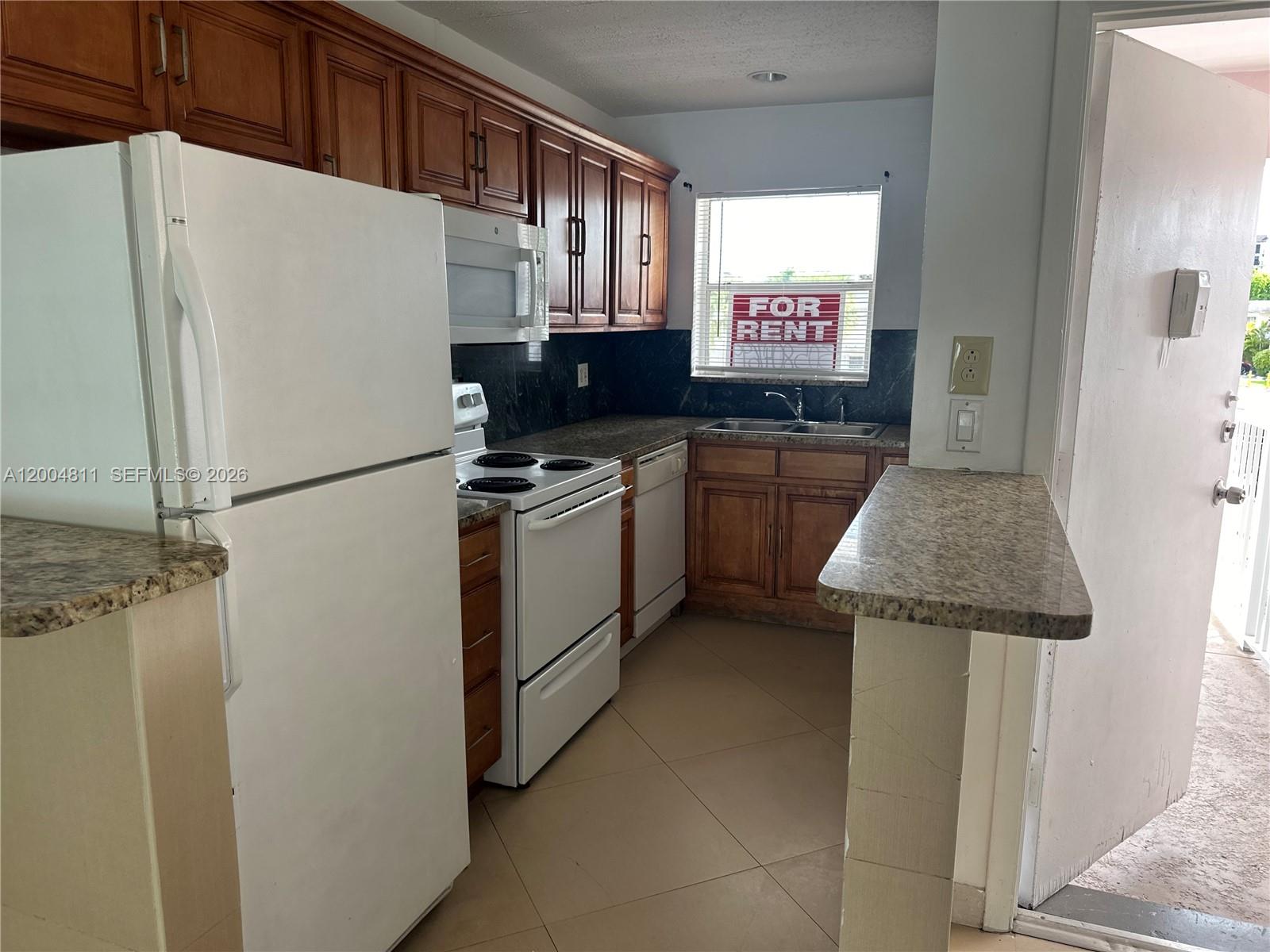 A kitchen features wood cabinets, granite countertops, white appliances, and a window with a sign — 7424 SW 82nd St # D216, Miami FL 33143, MIAMI, FL
