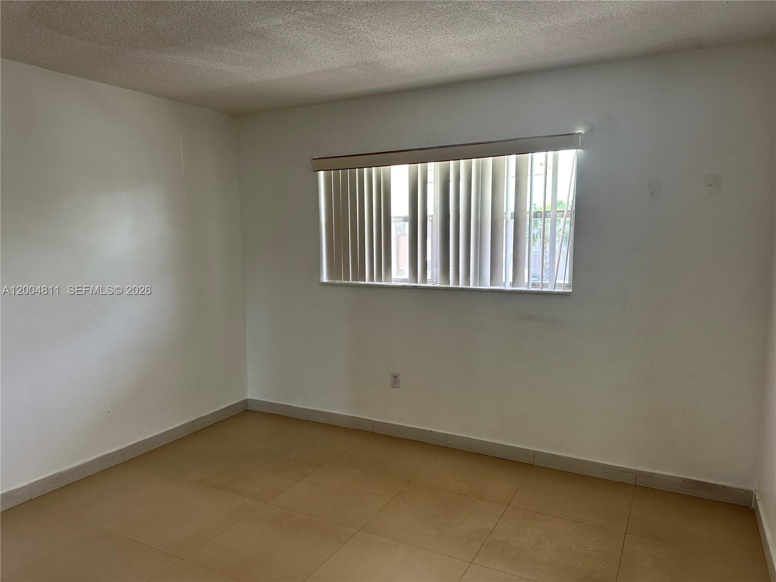 An empty room features white walls, tan tile flooring, and a window with vertical blinds — 7424 SW 82nd St # D216, Miami FL 33143, MIAMI, FL