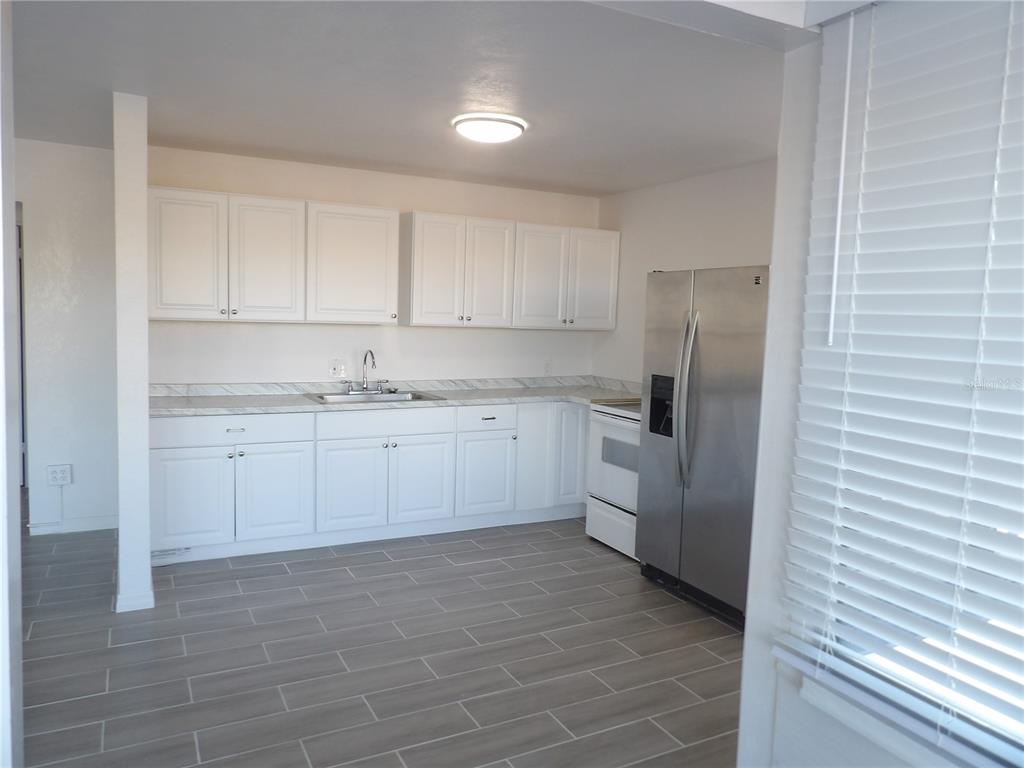 A kitchen features white cabinets, marble-look countertops, stainless steel appliances, and gray tile flooring — 14975 1ST STREET E, MADEIRA BEACH, FL