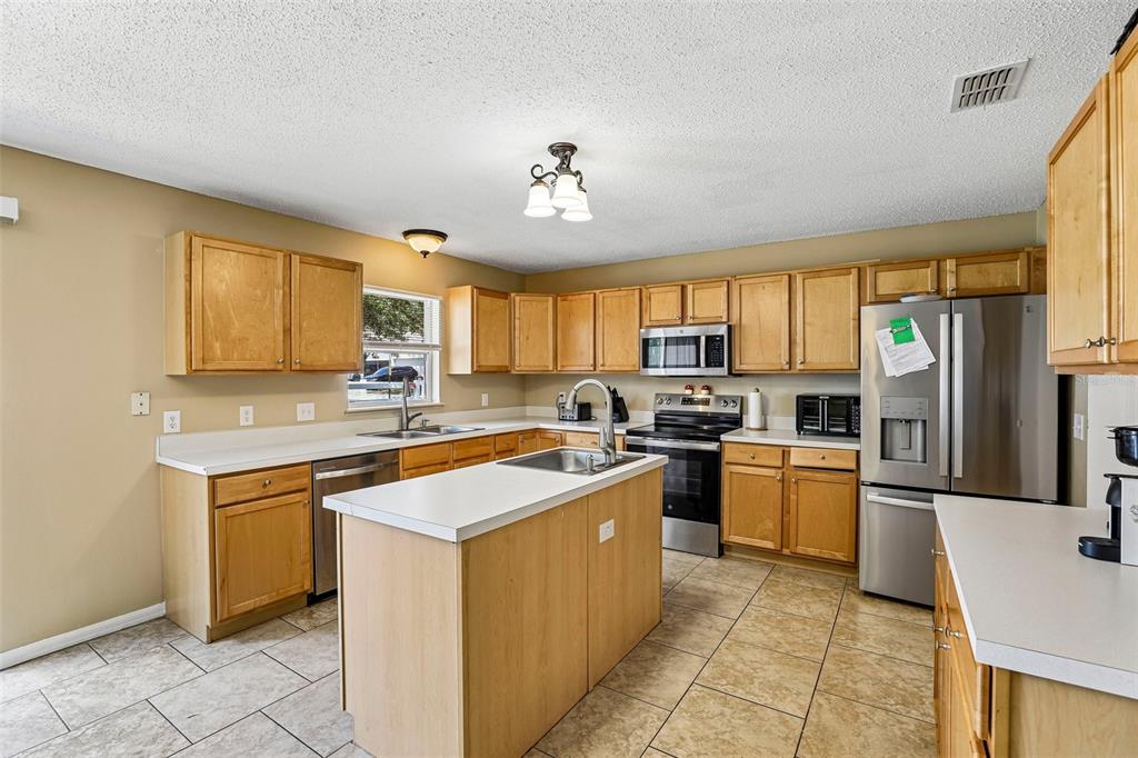A kitchen features light wood cabinets, white countertops, stainless steel appliances, and tiled flooring — 274 JOCELYN DRIVE, DAVENPORT, FL