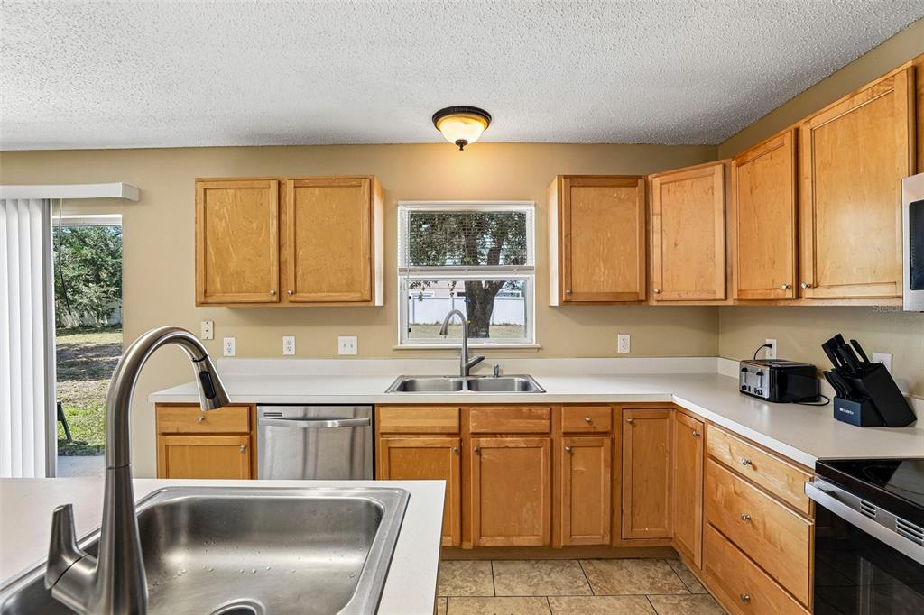 A kitchen features light wood cabinets, white countertops, stainless steel appliances, and a window — 274 JOCELYN DRIVE, DAVENPORT, FL