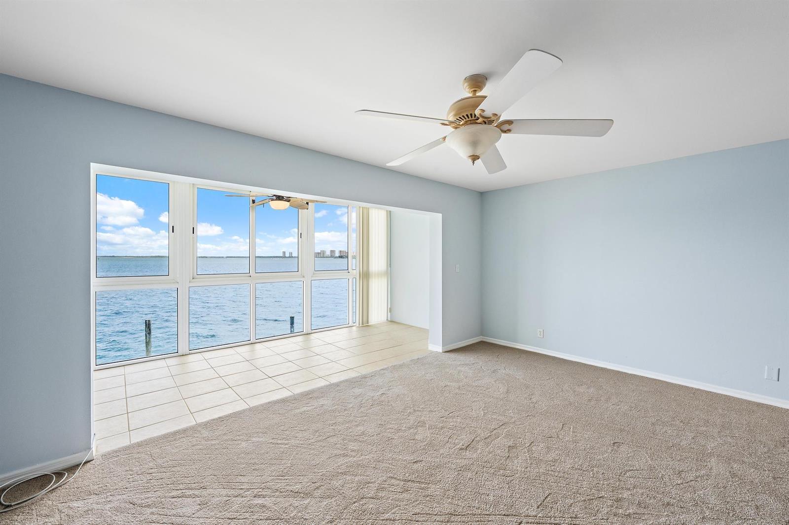 An empty room with light blue walls, beige carpeting, a ceiling fan, and floor-to-ceiling windows — 400 Wilma Circle # 206, Riviera Beach FL 33404, RIVIERA BEACH, FL