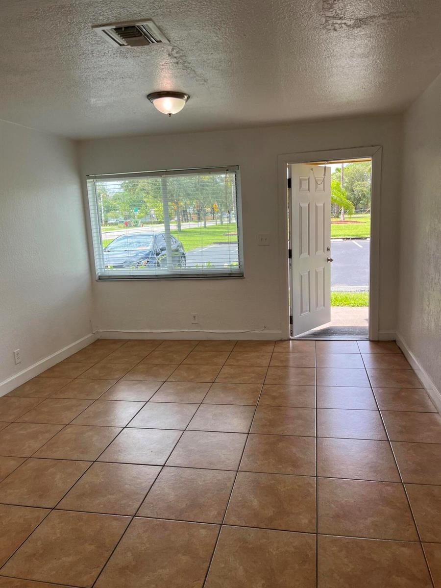 An empty room with tan tile flooring, a window with blinds, and an open door — 610 NW 7th Avenue, Pompano Beach FL 33060, POMPANO BEACH, FL