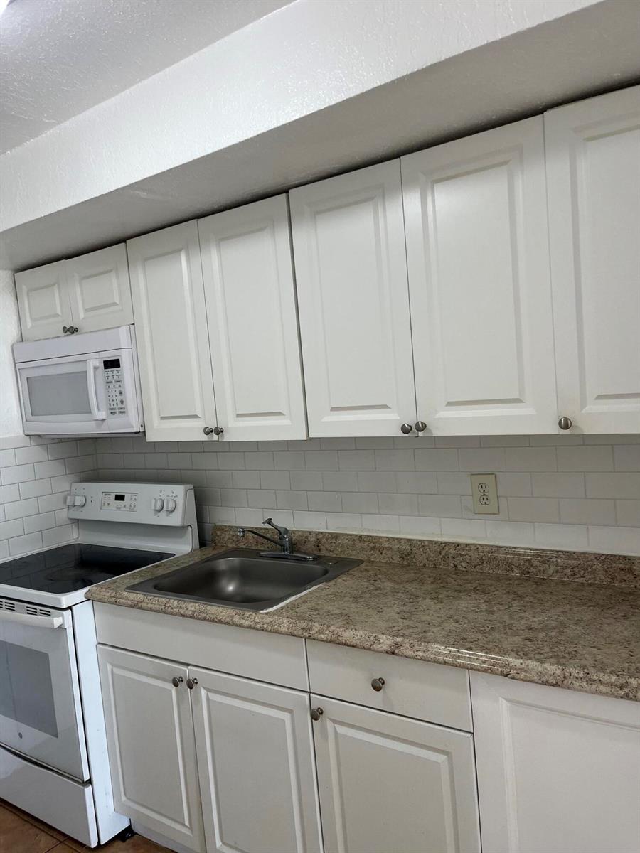 A kitchen features white cabinets, a speckled countertop, a stainless steel sink, and white appliances — 610 NW 7th Avenue, Pompano Beach FL 33060, POMPANO BEACH, FL