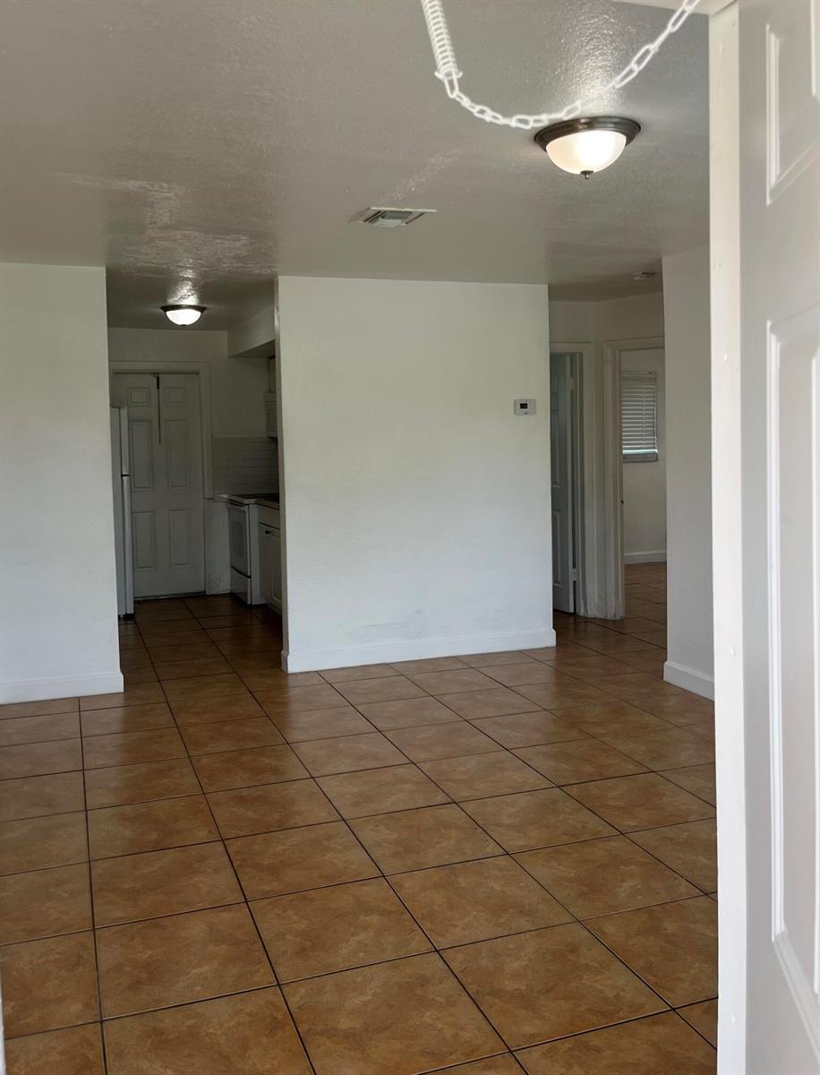 An interior view shows a living area with brown tile flooring and a kitchen beyond — 610 NW 7th Avenue, Pompano Beach FL 33060, POMPANO BEACH, FL