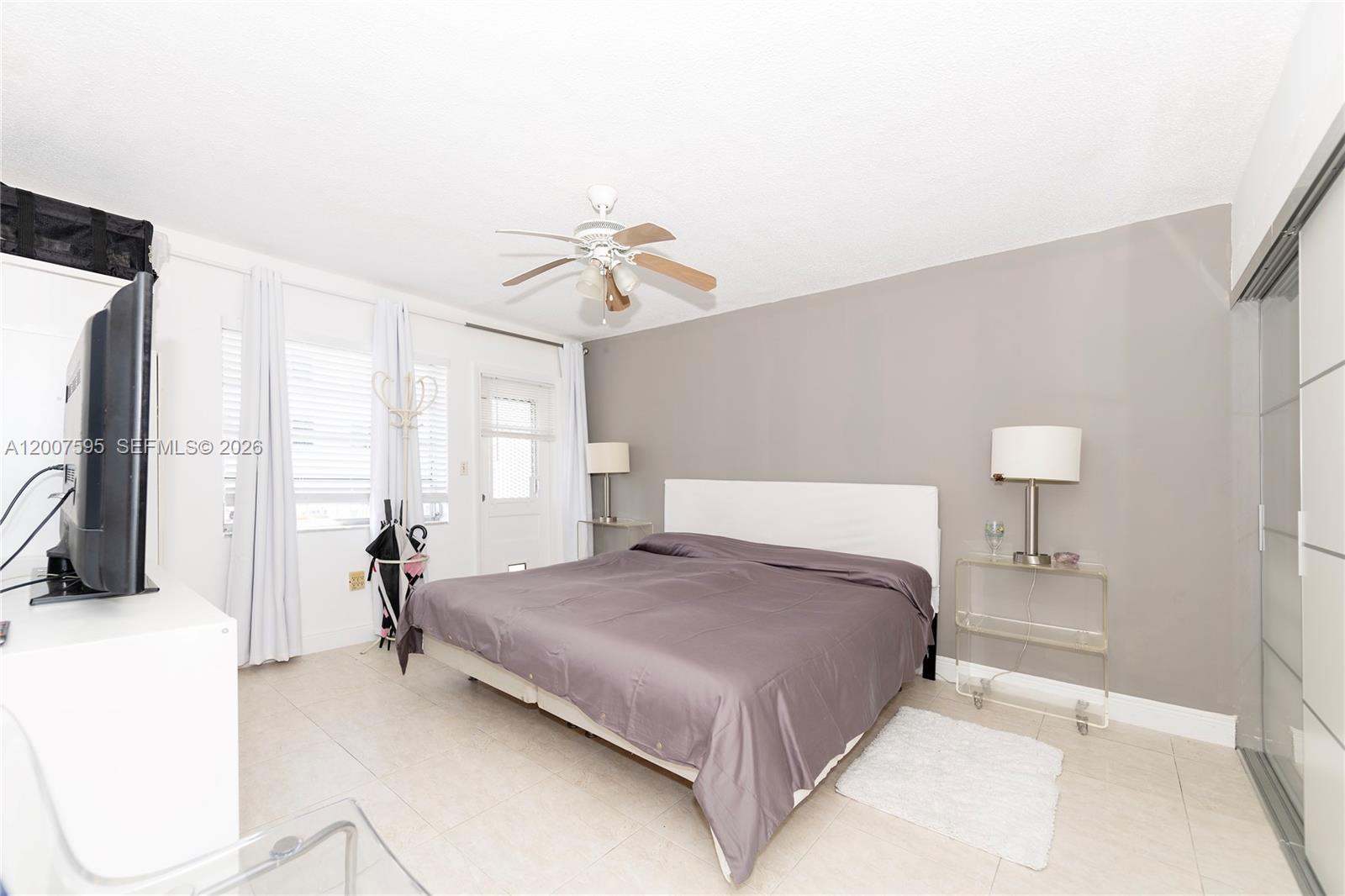 A bedroom features a bed with a grey comforter, a ceiling fan, and tile flooring — MIAMI BEACH, FL