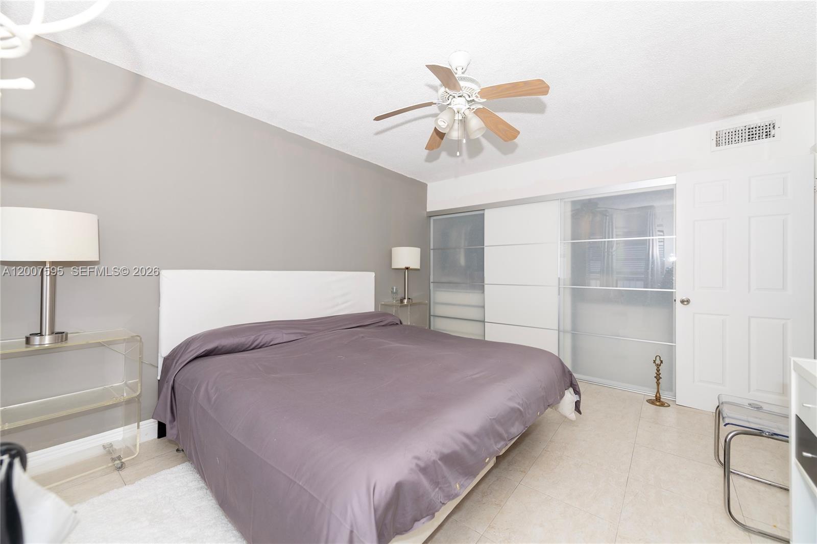A bedroom features a bed with a purple comforter, sliding closet doors, and a ceiling fan — MIAMI BEACH, FL