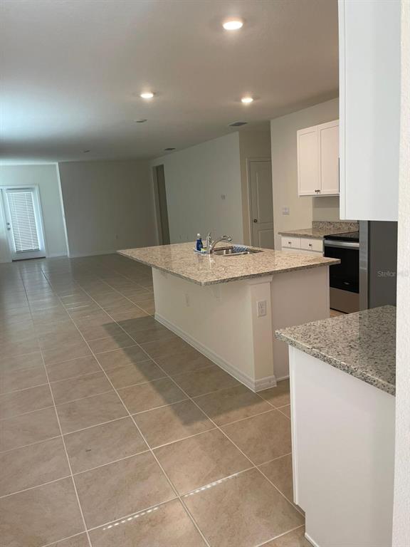 A kitchen features a granite-topped island, white cabinetry, and light-colored tile flooring — 927 WATERFALL BOULEVARD, DAVENPORT, FL