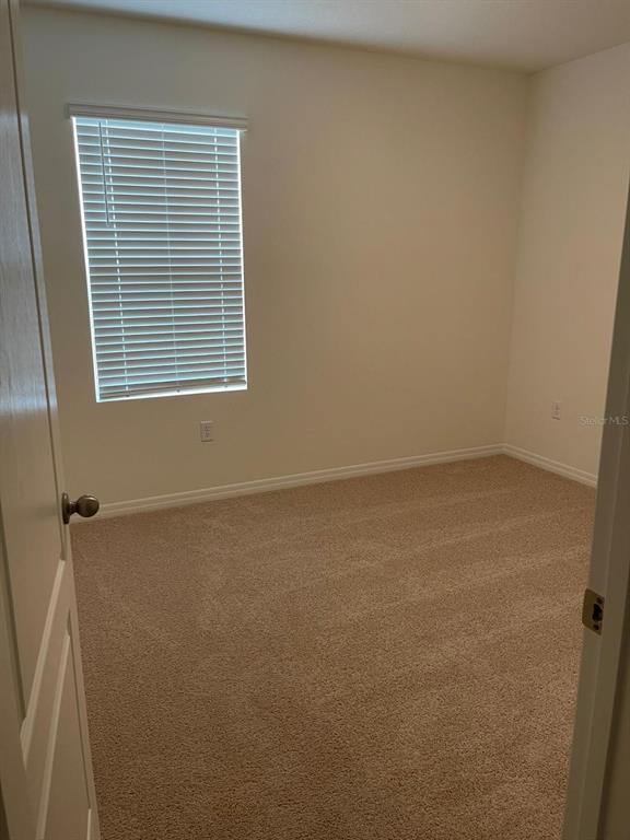An empty bedroom features beige carpet, off-white walls, and a window with white blinds — 927 WATERFALL BOULEVARD, DAVENPORT, FL