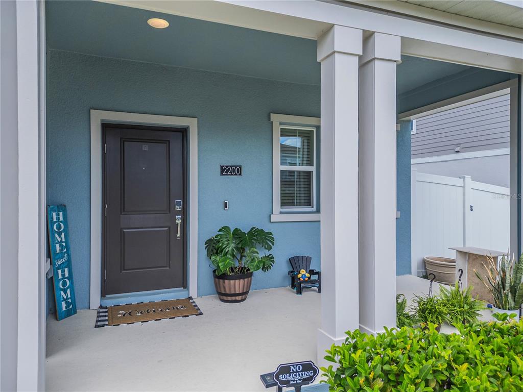 A blue-painted front porch features a dark door, a potted plant, and a welcome mat — 2200 SWEET HONEY LANE, APOPKA, FL