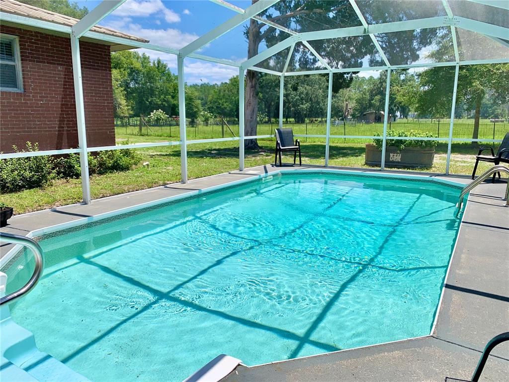 A swimming pool enclosed by a screen cage sits next to a red brick house — 15770 NW 60TH AVENUE, CHIEFLAND, FL