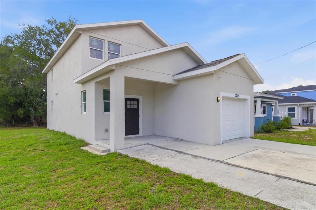 A two-story, light-colored stucco house features a single-car garage and a covered front entryway — 3702 WIGGINS LEAF STREET, TAMPA, FL