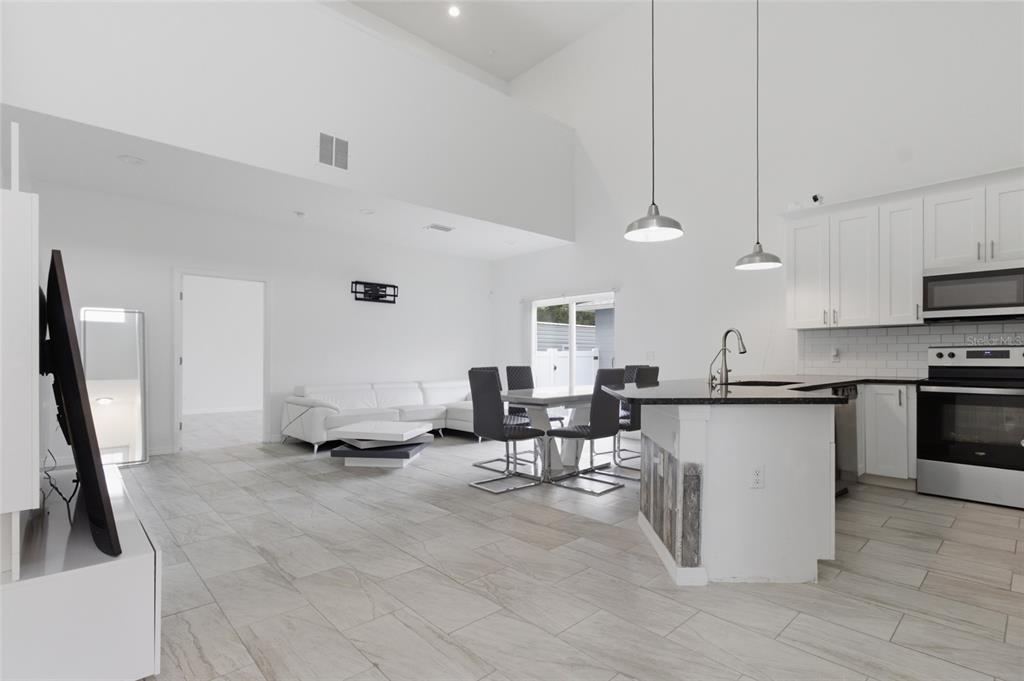 An open-concept kitchen and living area with white cabinets, tile floors, and vaulted ceilings — 3702 WIGGINS LEAF STREET, TAMPA, FL