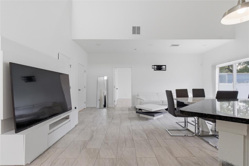 A bright, open-concept living and dining area features white walls, tile flooring, and modern furniture — 3702 WIGGINS LEAF STREET, TAMPA, FL
