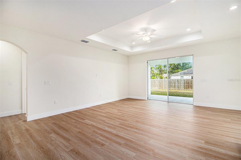 A bright living room features light wood-look flooring, a tray ceiling, and sliding glass doors — 801 GELASO STREET SW, PALM BAY, FL
