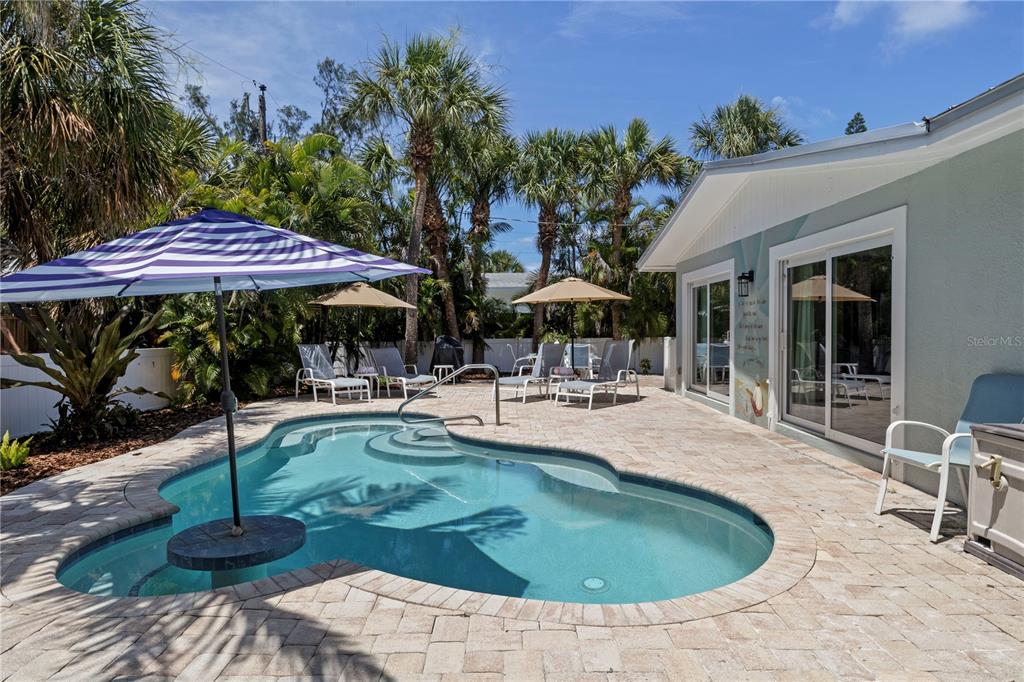 A backyard features a swimming pool with a blue umbrella and patio lounge chairs — 110 PALM AVENUE, ANNA MARIA, FL