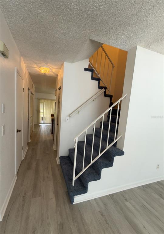 A staircase with blue carpet and white railings sits beside a hallway with wood-look flooring — 6630 121ST AVENUE UNIT 6, LARGO, FL