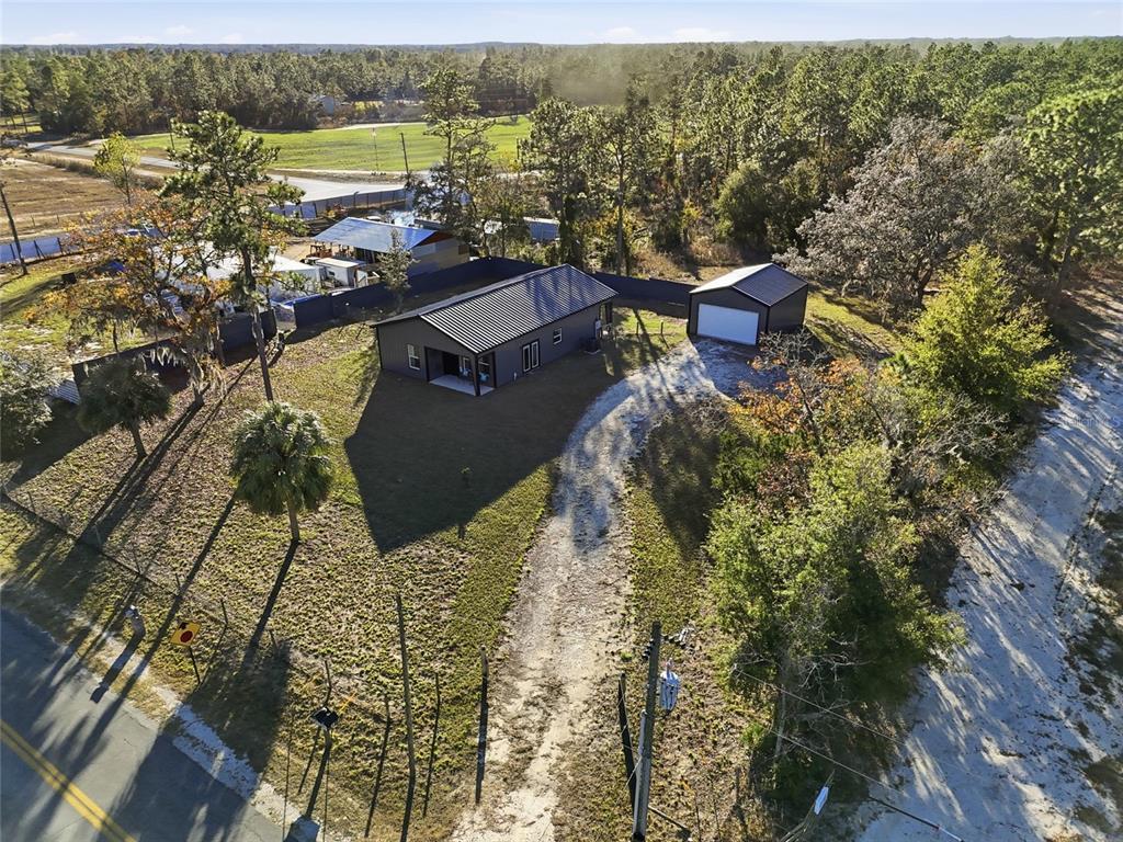 An aerial view shows a dark-sided house and a detached garage on a wooded lot — 4030 NE 140TH COURT, WILLISTON, FL