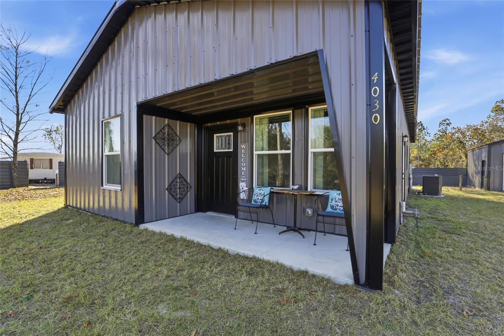 A modern metal-sided house features a covered concrete porch with two chairs and a table — 4030 NE 140TH COURT, WILLISTON, FL