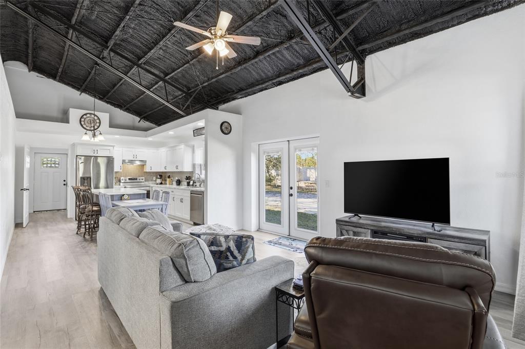 A living room with a vaulted black ceiling, gray sofa, and an open-concept white kitchen — 4030 NE 140TH COURT, WILLISTON, FL