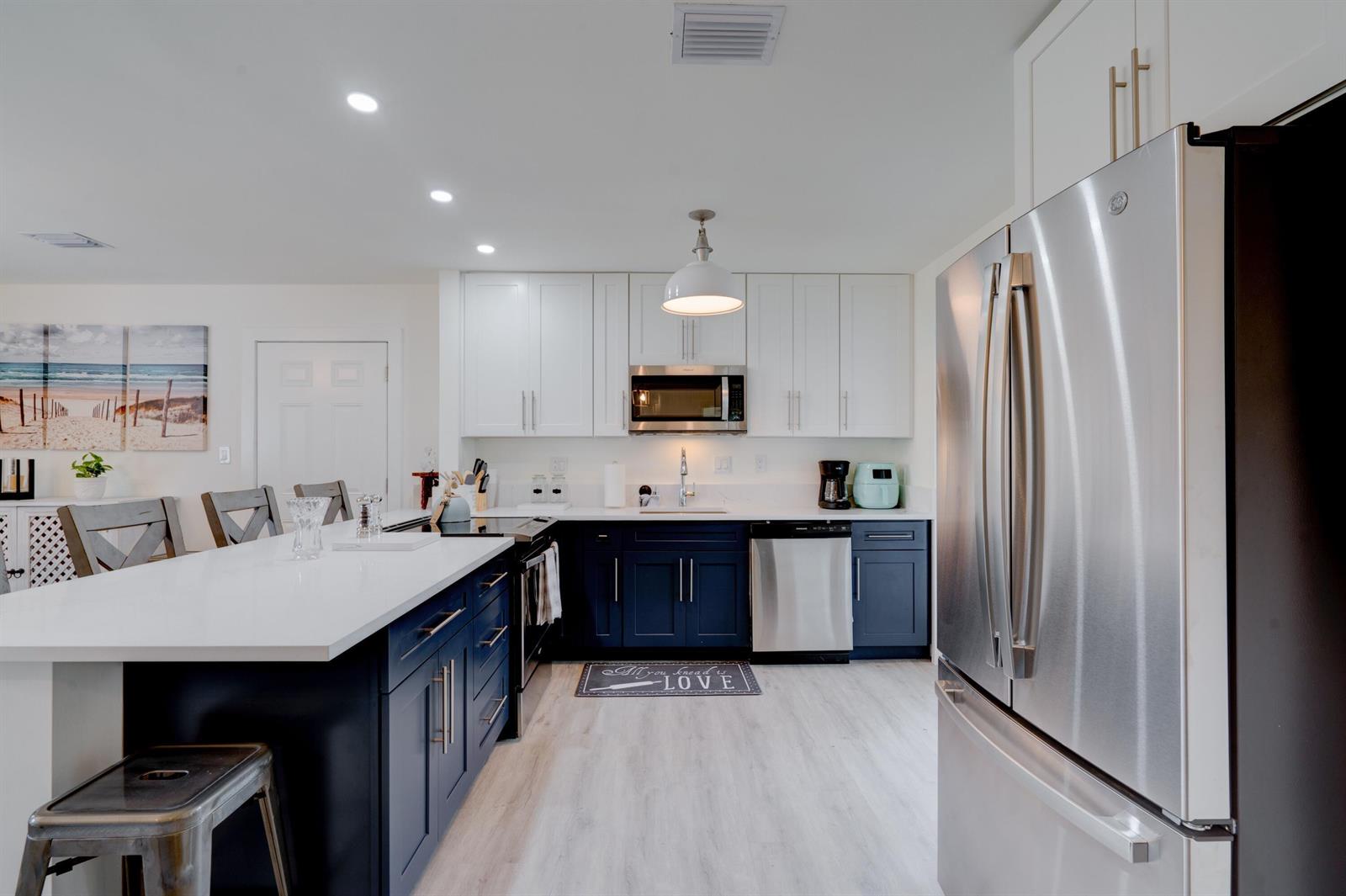 A modern kitchen features white upper cabinets, dark blue lower cabinets, and a white island — 1036 Coral Drive, Boynton Beach FL 33426, BOYNTON BEACH, FL