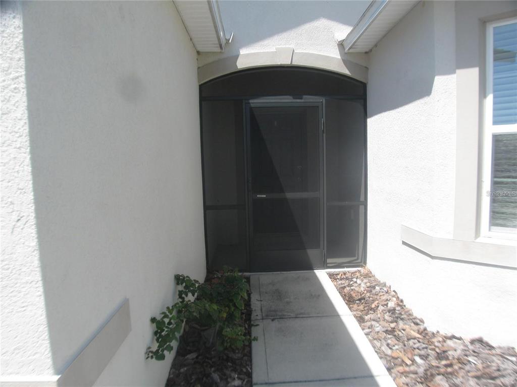 A concrete walkway leads to a front entryway with a black screen door — 599 AUTUMN STREAM DRIVE, AUBURNDALE, FL