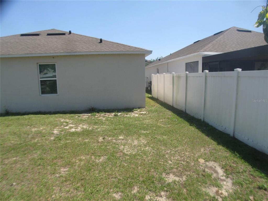 A side view of a house exterior with a white vinyl fence in the backyard — 599 AUTUMN STREAM DRIVE, AUBURNDALE, FL