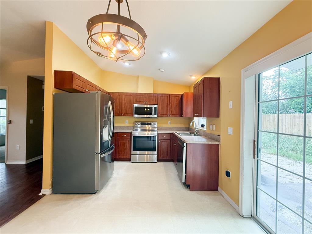 A kitchen features wood cabinets, stainless steel appliances, and a sliding glass door — 11740 RANCHO DRIVE, LEESBURG, FL