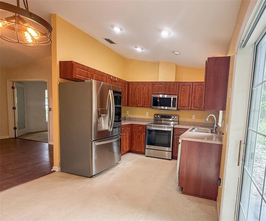 A kitchen features wood cabinets, stainless steel appliances, and tile flooring — 11740 RANCHO DRIVE, LEESBURG, FL