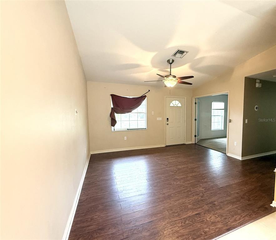 A living room with wood-look flooring, a ceiling fan, and a front entry door — 11740 RANCHO DRIVE, LEESBURG, FL