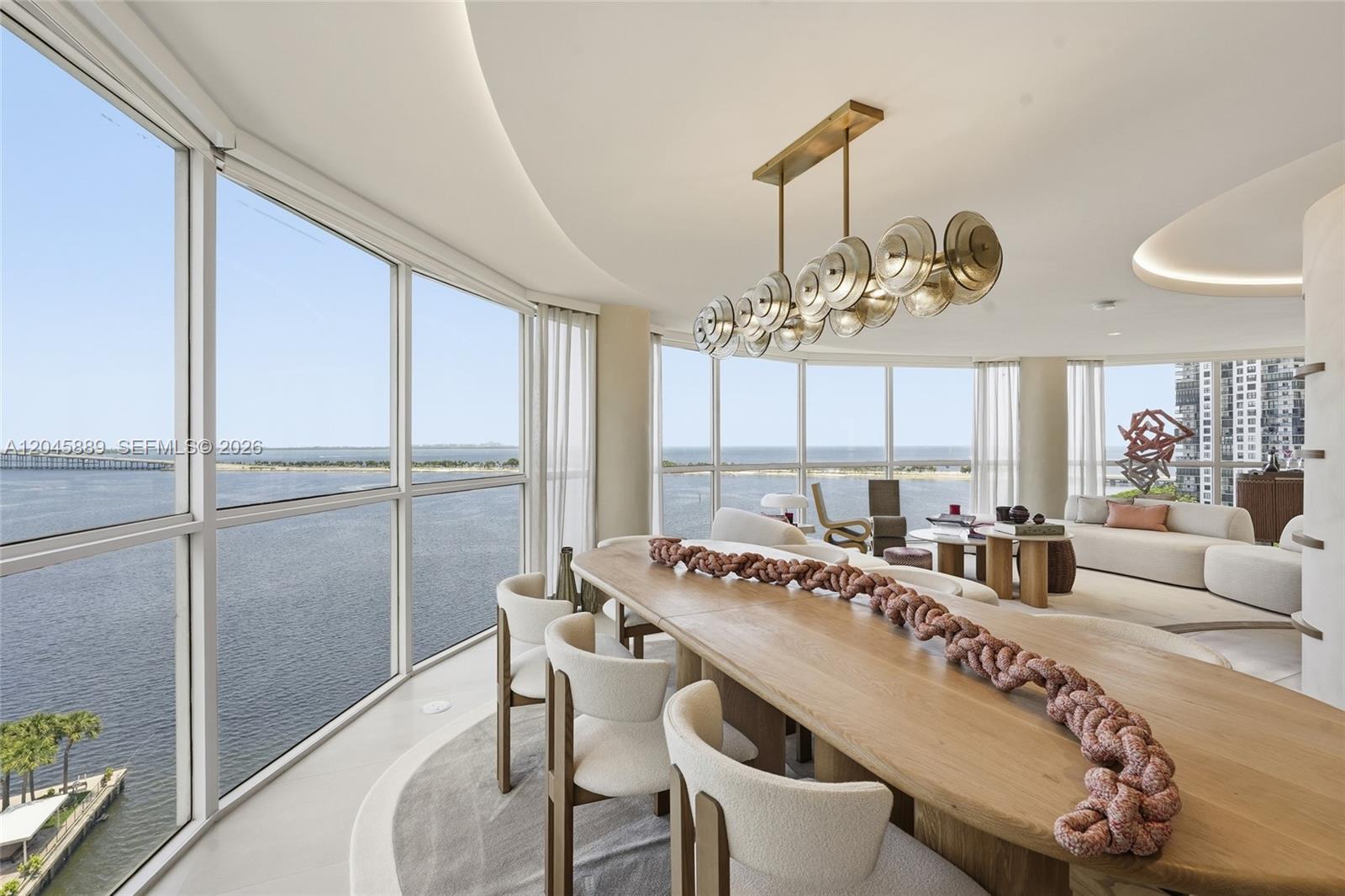 A dining room with a long wooden table, modern chandelier, and floor-to-ceiling ocean views — 2025 Brickell Ave # 1401, Miami FL 33129, MIAMI, FL
