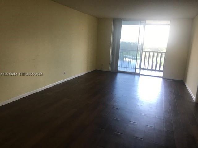 An empty living room features dark wood-look flooring and a sliding glass door to a balcony — 3001 W Rolling Hills Cir # 701, Davie FL 33328, DAVIE, FL