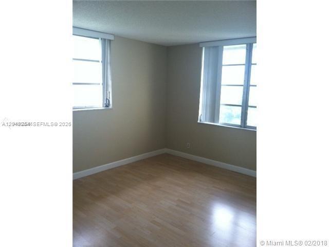 An empty room features light wood-look flooring, beige walls, and two windows with blinds — 3001 W Rolling Hills Cir # 701, Davie FL 33328, DAVIE, FL