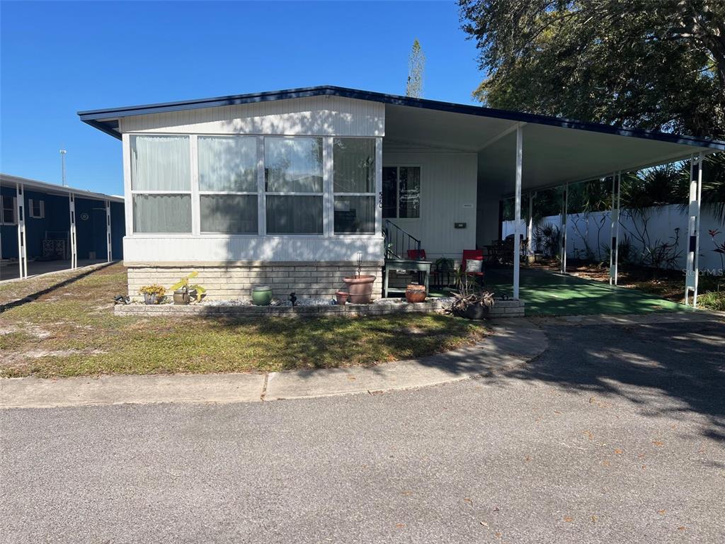 A single-story manufactured home features a large front window, a brick base, and a carport — 29250 US HIGHWAY 19 N UNIT 570, CLEARWATER, FL