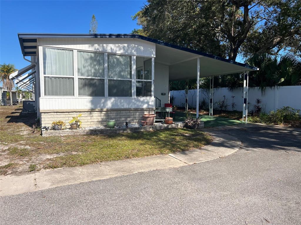 A single-story manufactured home features a white exterior, a carport, and a brick-accented front garden — 29250 US HIGHWAY 19 N UNIT 570, CLEARWATER, FL