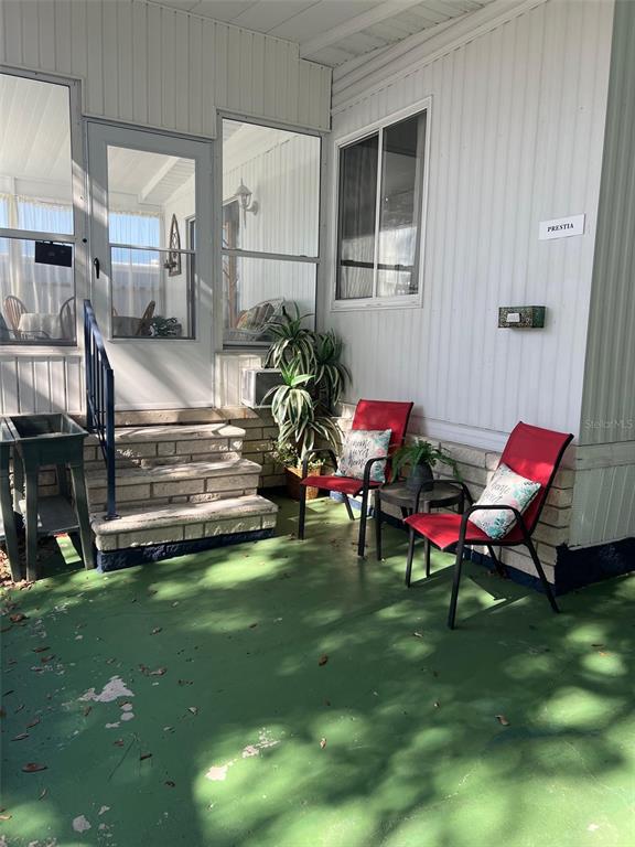 A covered porch features a green floor, brick steps, two red chairs, and a plant — 29250 US HIGHWAY 19 N UNIT 570, CLEARWATER, FL