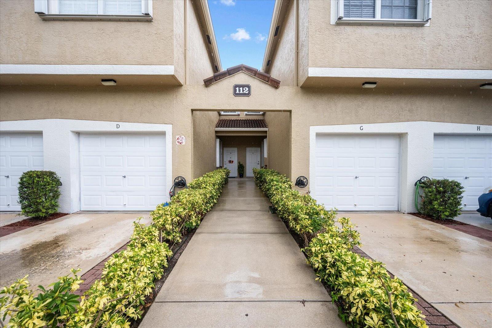 An exterior view of a multi-unit residential building with garage doors and a central walkway — 112 Lighthouse Circle # G, Tequesta FL 33469, TEQUESTA, FL