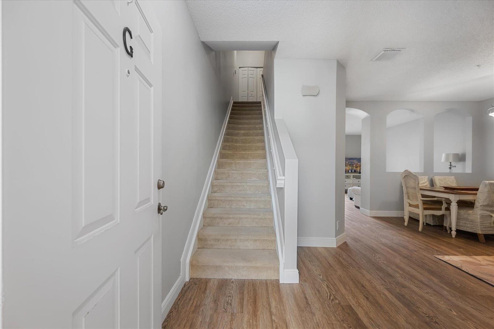 An entryway features a carpeted staircase, light gray walls, and wood-look flooring — 112 Lighthouse Circle # G, Tequesta FL 33469, TEQUESTA, FL