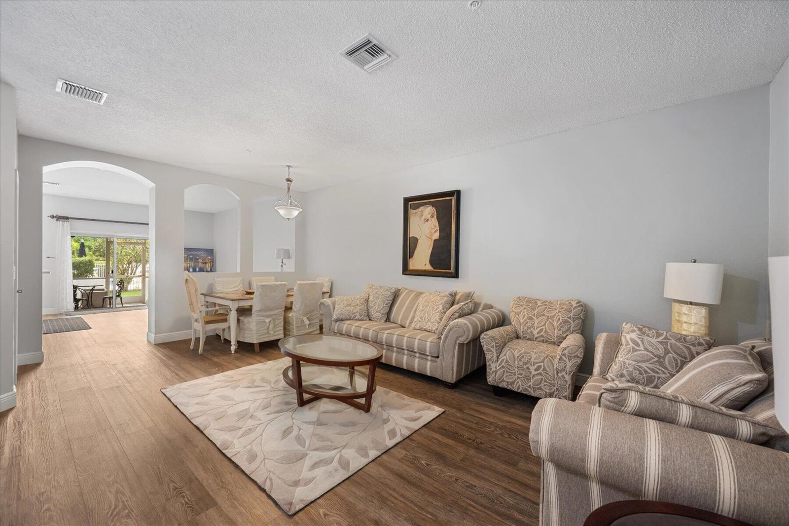 A living room with wood-look flooring, a striped sofa, patterned armchairs, and a dining area — 112 Lighthouse Circle # G, Tequesta FL 33469, TEQUESTA, FL