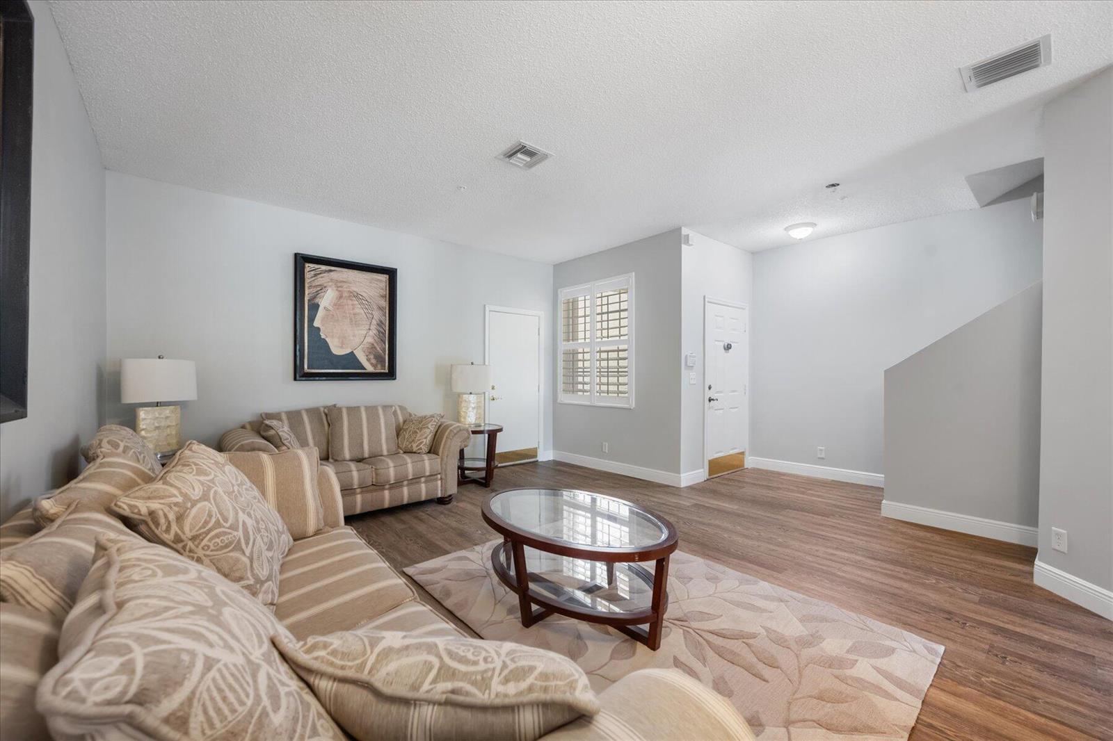 A living room features light gray walls, wood-look flooring, two striped sofas, and a coffee table — 112 Lighthouse Circle # G, Tequesta FL 33469, TEQUESTA, FL