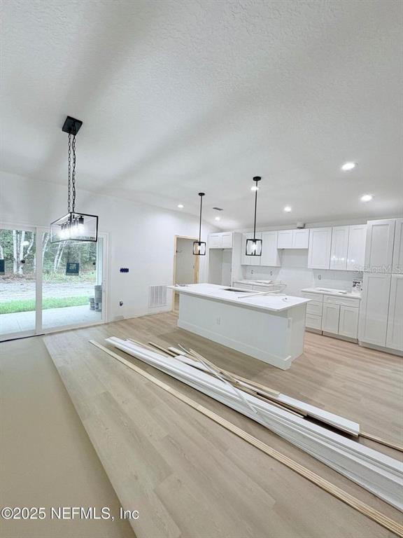 A kitchen with white cabinets, a central island, and light wood flooring under construction — 1264 CORAL FARMS ROAD, FLORAHOME, FL