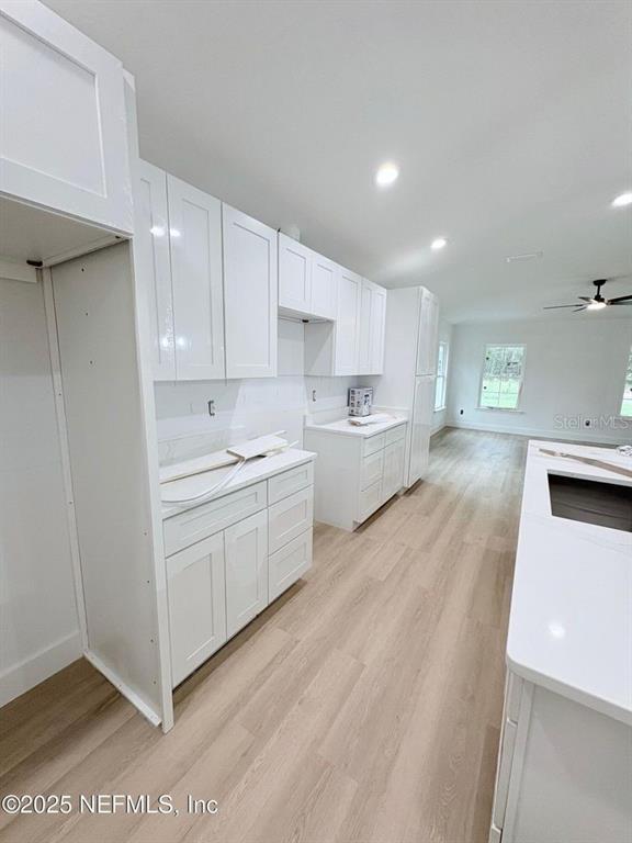 A modern kitchen features white cabinets, light wood-look flooring, and a large central island — 1264 CORAL FARMS ROAD, FLORAHOME, FL