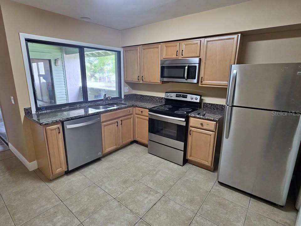 A kitchen features light wood cabinets, stainless steel appliances, granite countertops, and tile flooring — 4158 PINELAKE LANE UNIT 202, TAMPA, FL