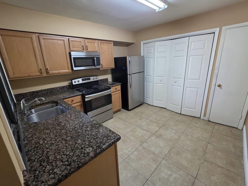 A kitchen features wood cabinets, granite countertops, stainless steel appliances, and light-colored floor tiles — 4158 PINELAKE LANE UNIT 202, TAMPA, FL