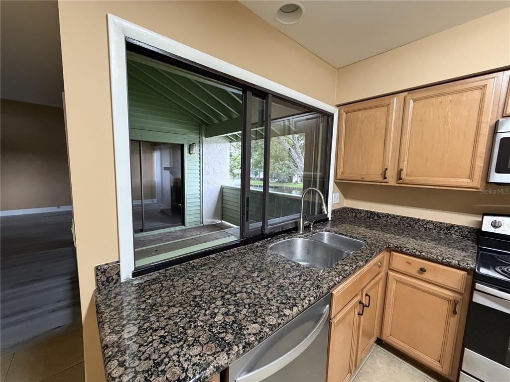 A kitchen features granite countertops, light wood cabinets, a stainless steel sink, and a window — 4158 PINELAKE LANE UNIT 202, TAMPA, FL