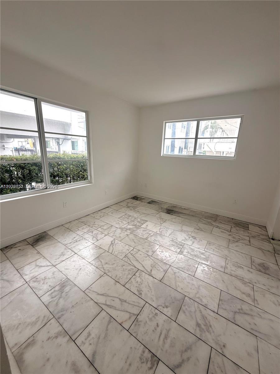 An empty room features white walls, large windows, and light-colored marble tile flooring — 922 Jefferson Ave # 6, Miami Beach FL 33139, MIAMI BEACH, FL